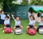 Happy children in school uniforms sitting on toy cars in a playground with excited expressions as they raise their hands Starshine Montessori 90x80