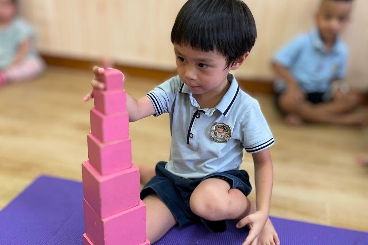A child carefully stacking pink blocks on a purple mat in a classroom
