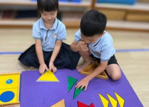 Children in uniforms play with shape puzzles on a purple mat in a classroom