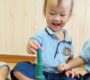 Smiling toddler stacking green blocks in school uniform indoor playtime activity Starshine Montessori 90x80