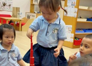 Young children in a classroom stacking red blocks while sitting together and focusing on the Montessori activity at Starshine Montessori.