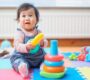 Baby playing with colorful stacking toy on mat 90x80