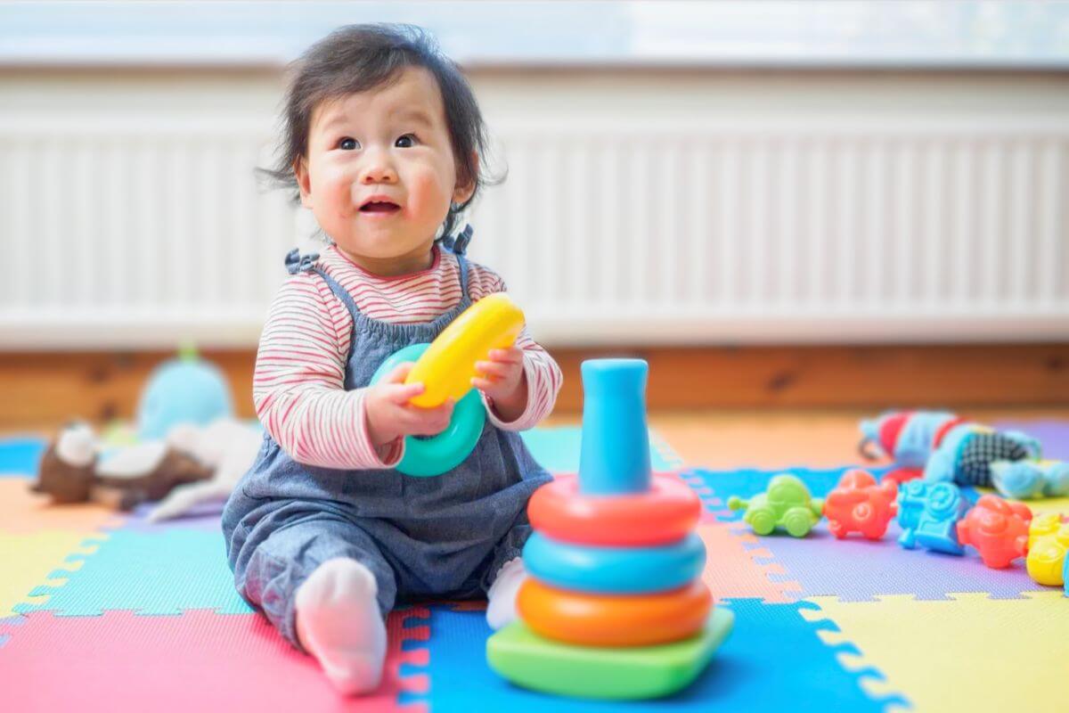 Smiling baby playing with colorful stacking rings on a foam play mat in a bright indoor environment, encouraging early learning and motor skill development.