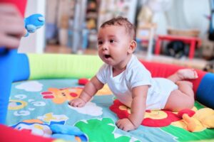 Smiling baby enjoying tummy time on a colorful playmat, supporting early motor development and sensory exploration.