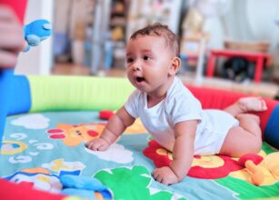 Smiling baby enjoying tummy time on a colorful playmat, supporting early motor development and sensory exploration.