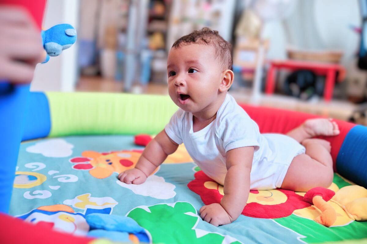 Smiling baby enjoying tummy time on a colorful playmat, supporting early motor development and sensory exploration.