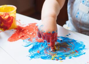 Close-up of a toddler engaging in finger painting with vibrant red, blue, and yellow colors, promoting sensory and creative development.