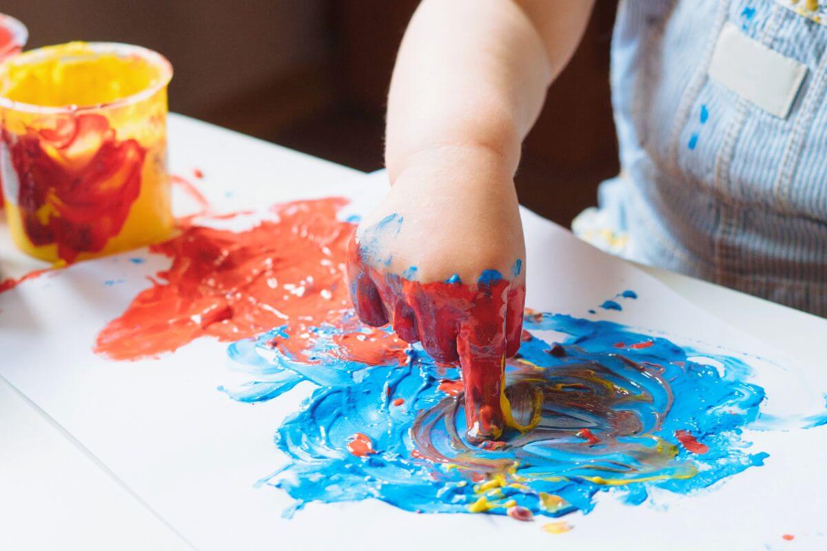 Close-up of a toddler engaging in finger painting with vibrant red, blue, and yellow colors, promoting sensory and creative development.