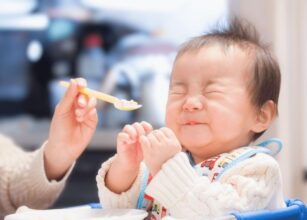 Adorable baby making a funny face during feeding time, reacting to the first spoonful of food at home.