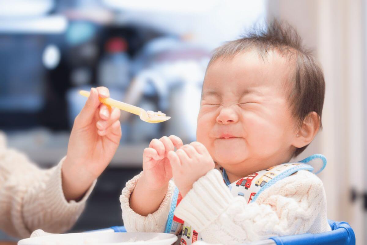 Adorable baby making a funny face during feeding time, reacting to the first spoonful of food at home.