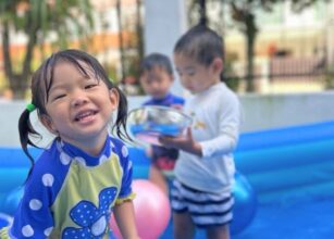 Smiling preschool girl in blue polka dot rash guard enjoying water play in an inflatable pool with other children at Starshine Montessori Hillview.